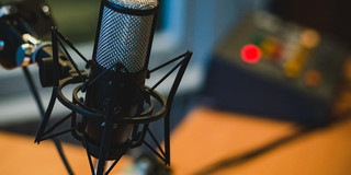 Ein hochwertiges Mikrofon steht bereit, um klare und präzise Klänge aufzunehmen. Mit seinem feinen Netzkorb und der stabilen Halterung ist es ideal für Aufnahmen im Studio oder Live-Performances. Im Hintergrund sind die Bedienelemente eines Mischpults sichtbar, die darauf warten, das aufgenommene Audio zu optimieren. Die Atmosphäre ist geprägt von Kreativität und technischer Expertise.