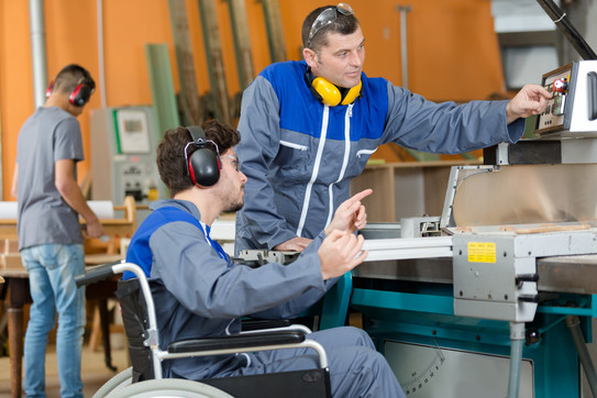 Person im Rollstuhl vor einer Fertigungsmaschine