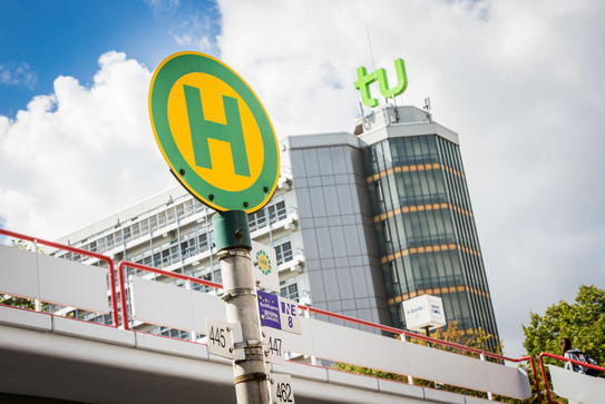 Bushaltestellenschild vor TU Dortmund Gebäude Bushaltestellenschild mit Mensabrücke und Mathetower im Hintergrund.